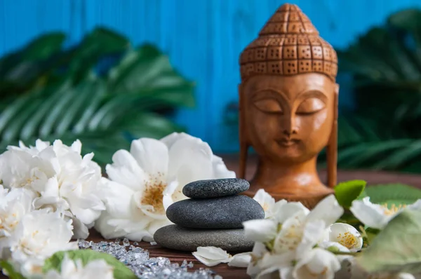 Gri Zen taşlarından piramitler, güzel taze beyaz çiçekler yeşil yapraklar ve ahşap arka planda Buda heykeli. Uyum kavramı, denge ve meditasyon, spa, masaj, rahatlama