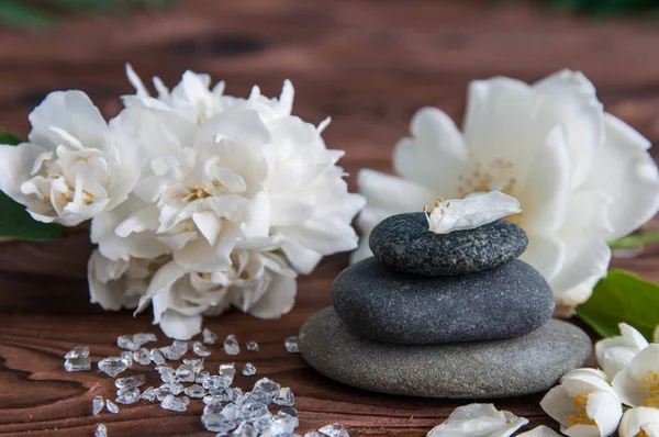 Gri Zen taşlarından piramitler, güzel taze beyaz çiçekler, ahşap arka planda yeşil yapraklar. Uyum kavramı, denge ve meditasyon, spa, masaj, rahatlama