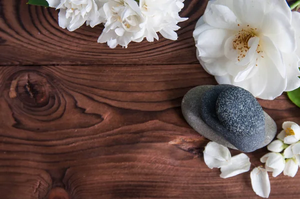 Gri Zen taşlarından piramitler, güzel taze beyaz çiçekler, ahşap arka planda yeşil yapraklar. Uyum kavramı, denge ve meditasyon, spa, masaj, rahatlama