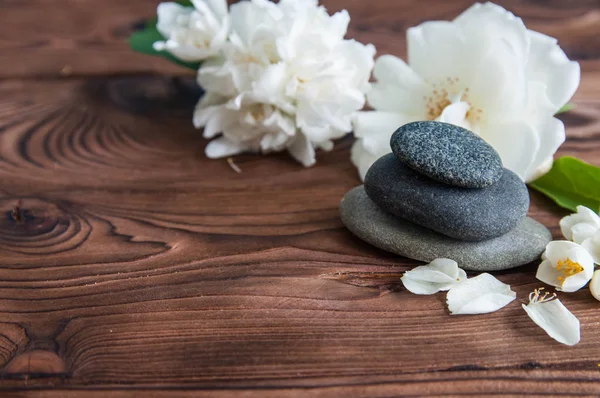Gri Zen taşlarından piramitler, güzel taze beyaz çiçekler, ahşap arka planda yeşil yapraklar. Uyum kavramı, denge ve meditasyon, spa, masaj, rahatlama