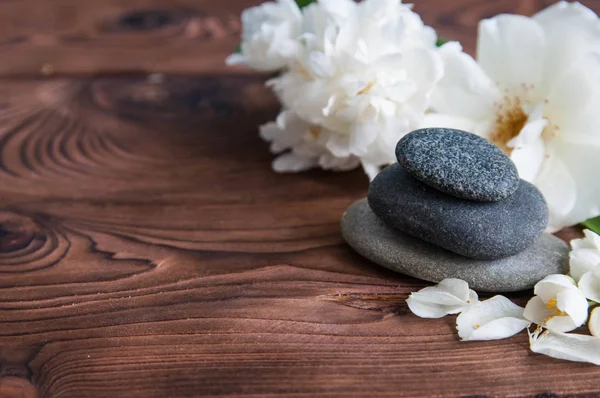 Pyramids of gray zen stones with beautiful fresh white flowers green leaves on wooden background. Concept of harmony, balance and meditation, spa, massage, relax