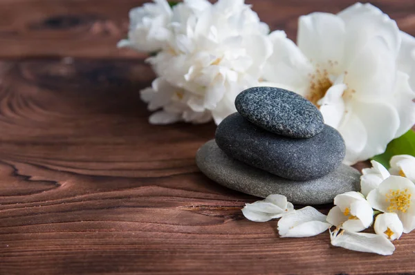 Gri Zen taşlarından piramitler, güzel taze beyaz çiçekler, ahşap arka planda yeşil yapraklar. Uyum kavramı, denge ve meditasyon, spa, masaj, rahatlama