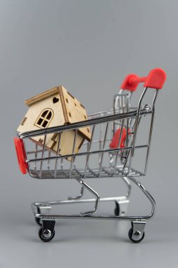 Ev almak, bina onarımı ve ipotek konsepti. Tahmini gayrimenkul, kredi parası ve bankacılık. Gri arka planda alışveriş arabasında bir ev.