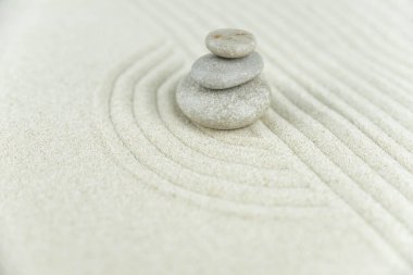 Zen bahçesi. Beyaz ve gri Zen taşlarından piramitler soyut dalga çizimleriyle beyaz kumun üzerinde. Uyum kavramı, denge ve meditasyon, spa, masaj, rahatlama.