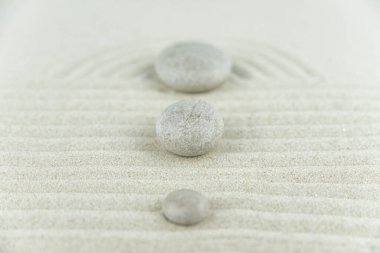 Zen bahçesi. Beyaz ve gri Zen taşlarından piramitler soyut dalga çizimleriyle beyaz kumun üzerinde. Uyum kavramı, denge ve meditasyon, spa, masaj, rahatlama.