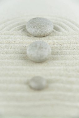 Zen bahçesi. Beyaz ve gri Zen taşlarından piramitler soyut dalga çizimleriyle beyaz kumun üzerinde. Uyum kavramı, denge ve meditasyon, spa, masaj, rahatlama.