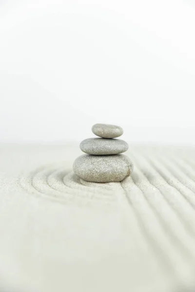 Zen bahçesi. Beyaz ve gri Zen taşlarından piramitler soyut dalga çizimleriyle beyaz kumun üzerinde. Uyum kavramı, denge ve meditasyon, spa, masaj, rahatlama.
