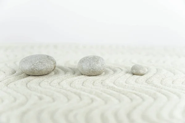 Zen bahçesi. Beyaz ve gri Zen taşlarından piramitler soyut dalga çizimleriyle beyaz kumun üzerinde. Uyum kavramı, denge ve meditasyon, spa, masaj, rahatlama.