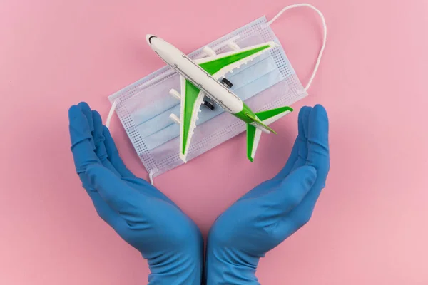 Safe travels concept. Plane with surgical medical mask in hands in gloves. Safety flight and travel during quarantine and lockdown.