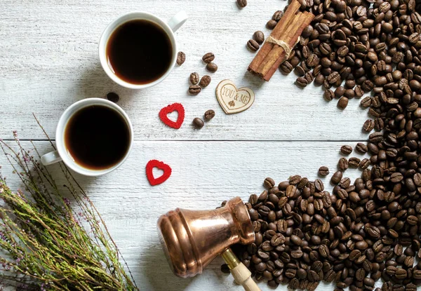 cups with coffee, cezve coffee grains,heather, hearts scattered on a light wooden background. Top view.