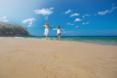 Beyaz elbiseli sevimli kızıyla genç ve güzel bir anne sahile yakın kumsalda yürüyor.