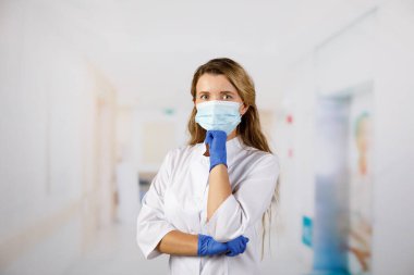 Doktor, koruyucu giysili bir kadın hastane koridorunda düşünceli bir şekilde duruyor. Coronavirus enfeksiyonu hayati tehlike arz ediyor.