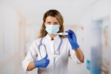 Termometre yakın planda. Doktor tıbbi dijital termometreyi tutar. Tıbbi maskeli bir doktor. Sıcaklık 36.6 iyileşmekte olan bir hastanın sembolü. Sağlık izleme için tanı ekipmanları.