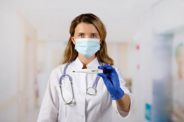 Termometre yakın planda. Doktor tıbbi dijital termometreyi tutar. Tıbbi maskeli bir doktor. Sıcaklık 36.6 iyileşmekte olan bir hastanın sembolü. Sağlık izleme için tanı ekipmanları.