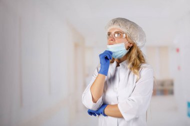 Doktor, koruyucu giysili bir kadın hastane koridorunda düşünceli bir şekilde duruyor. Coronavirus enfeksiyonu hayati tehlike arz ediyor.
