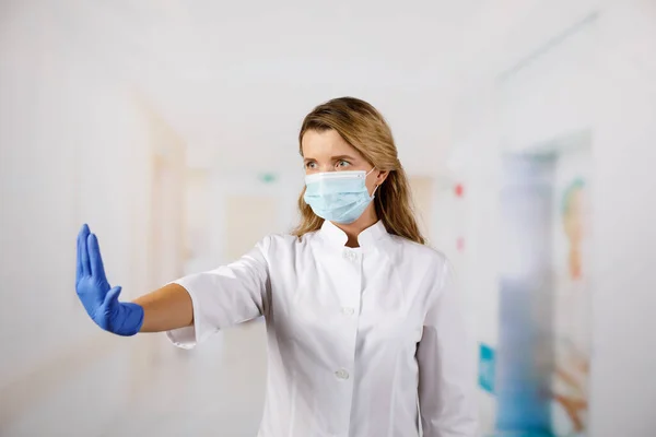 Female doctor in face mask showing stop sign with her hand