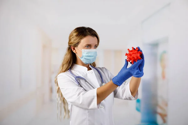 A masked female doctor holds a model 2019-nCoV (SARS-CoV-2). Chinese coronavirus disease COVID-19 is dangerous