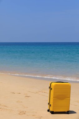 Kumsalda, mavi suların yanında sarı turist valizi..