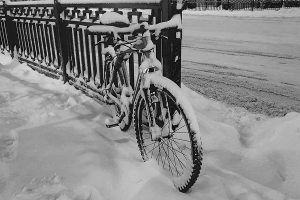 black and white snow-covered bike parked on the fence.