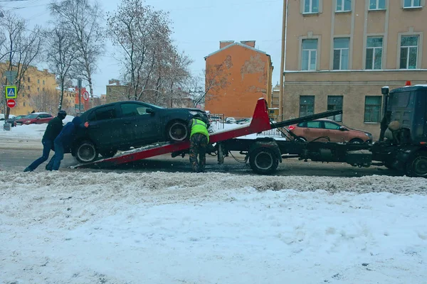 three men load a car on a tow truck during a snowfall