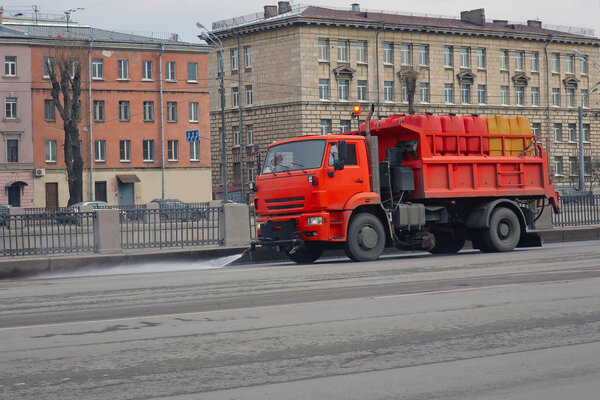 big orange watering machine washes the road part with water   