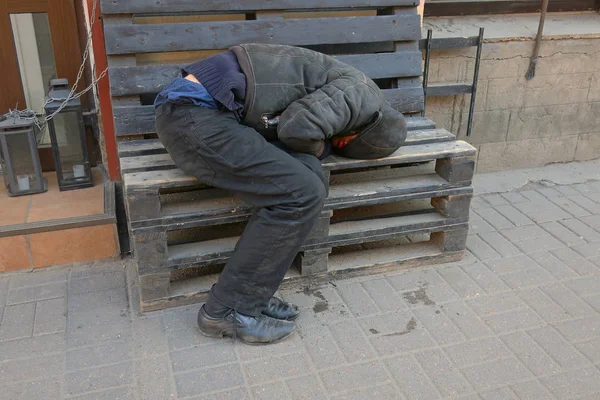 无家可归的睡在商店入口处的长凳上 — 图库照片