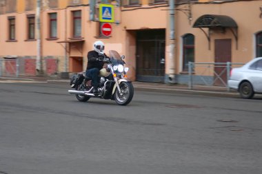 Beyaz kasklı bir adam şehir caddesinde motosikletsürüyor.