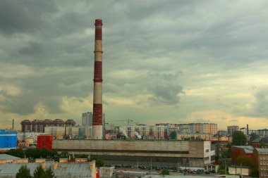 Bulutlu bir gökyüzüne karşı şehrin üzerinde yükselen eski uzun sanayi bacası