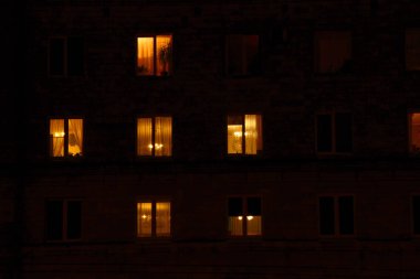 Gecenin karanlığında aydınlatılmış bir apartman evlerinin pencereleri