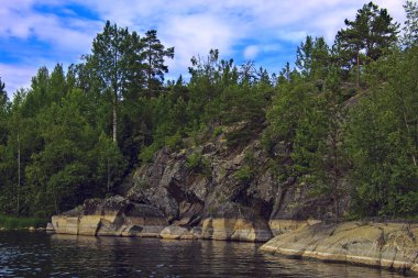 Karelia: bulutlu bir gökyüzü altında göl tarafından kayalar üzerinde orman
