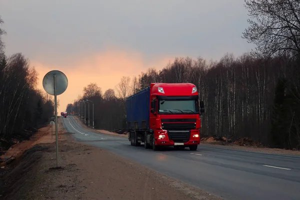 heavy truck moving along an asphalt forest road at sunset