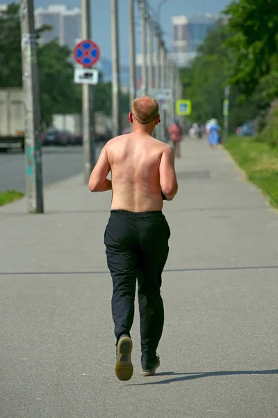 sweaty man with a naked torso running on the sidewalk