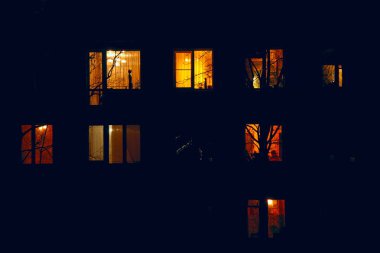 Gecenin karanlığında aydınlatılmış bir apartman evlerinin pencereleri