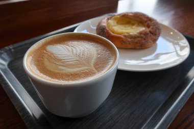 Bir fincan kahve broşür ve tepside bir fincan tabakta cheesecake ile süslenmiş.