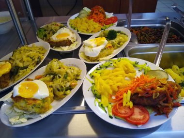 Halka açık bir yemek salonunda servis edilen oval tabaklarda sıcak yemekler.