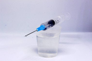 Ölçüm kabındaki şırınganın ucundaki iğneden sarkan bir aşı damlası