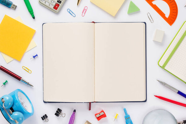 школьные принадлежности и открытая тетрадь или книга с пустыми страницами, вид сверху
