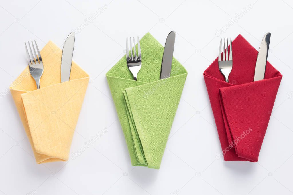 knife and fork in folded napkin at white background, top view