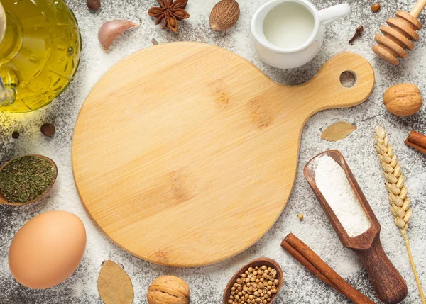 cutting board and bakery ingredients on wooden background, top view