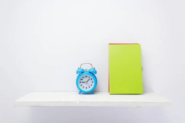 Notepad and alarm clock on shelf at white background — Stock Photo, Image