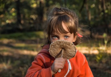 Güzel mavi gözlü beş-yıl-yaşlı kız şemsiye mantar elinde tutar. Sonbahar ormandır güzel çocuk.