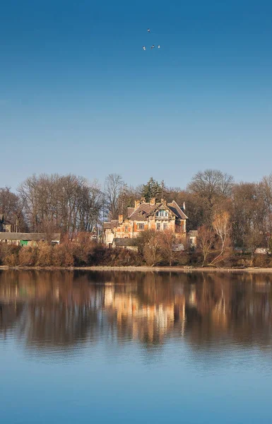 Old house over water. Reflection of a house in the river. Landscape with the house and trees displayed in the water