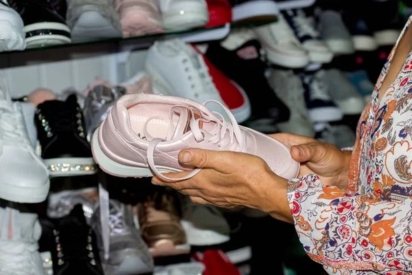 An elderly woman buys sneakers in a boutique. The choice of sports shoes in the store