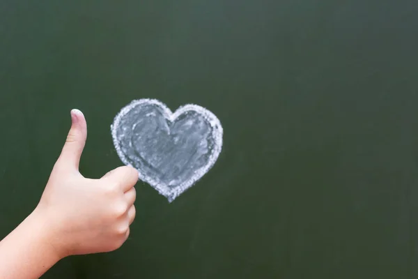 The girl shows by hand ok next to the heart drawn by the chalk on a blackboard. Congratulations on Valentine\'s Day. Free space for text