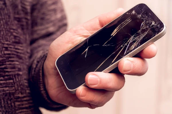 A man holds a phone with a broken glass in his hand. Phone repair service