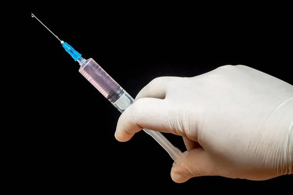 Injection syringe in doctor\'s hand on black isolated background