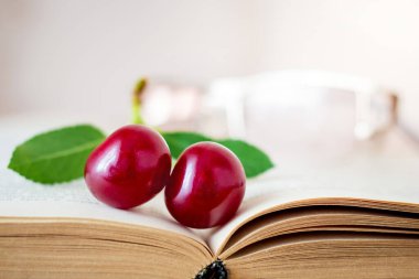 Kırmızı kiraz çileği ve bardaklar kitabın üzerinde. En sevdiğin kitabı okuyorum.