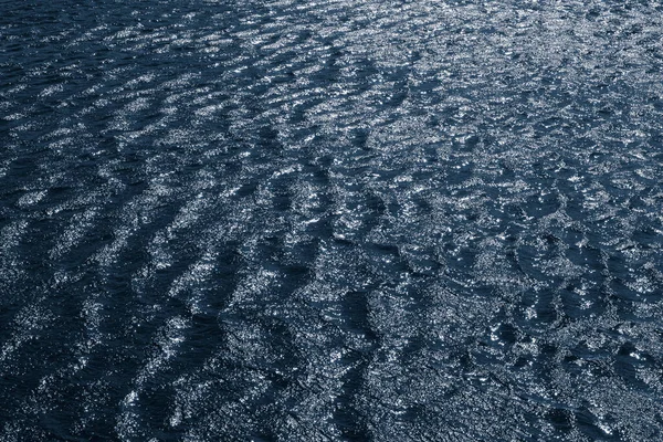 Background, texture from dark waves, in which the sun reflects. Dark waves on the surface of the river in windy weather