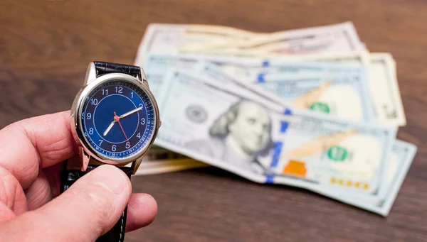 A man holds a clock in his hand against dollar bills. Time to earn money. Time is money. Copy space