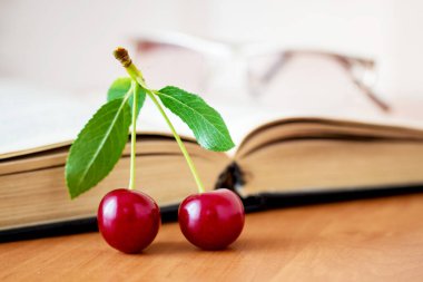 Açılmış kitabın yanındaki masada iki olgun kiraz